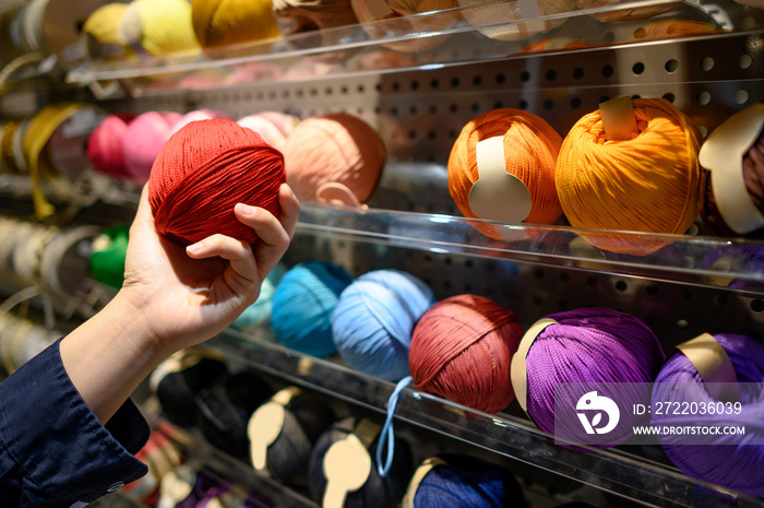 Male hand choosing red yarn ball in knitting shop or needlework shop. Selection of colorful yarn woo