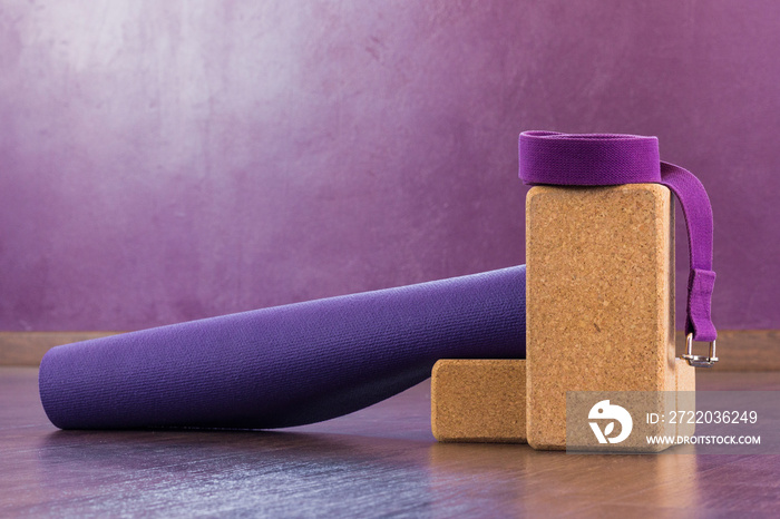 Yoga mat, cork bricks and purple strap on top. Studio props on wooden floor. Healthy lifestyle, work