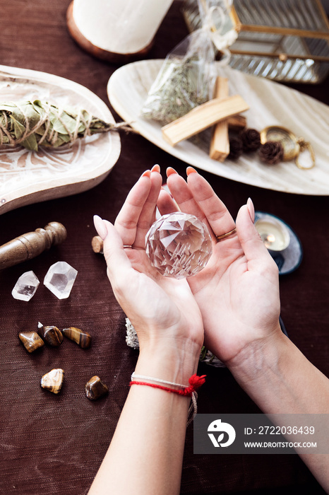 Detail of the hands of a woman with a crystal ball on a witch altar with several stones, crystals an