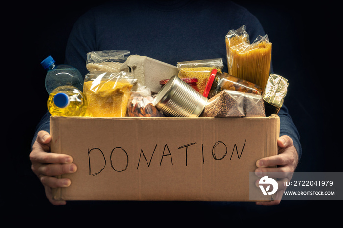 A man holding a donation box of different products on dark background