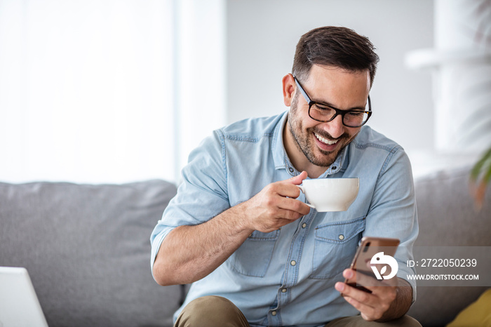 A smiling man makes a video call with friends while sitting on a sofa in his modern home. He uses a 