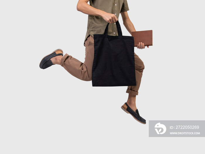 Man jump拿着袋子帆布织物，用于隔离在灰色背景上的模型空白模板。