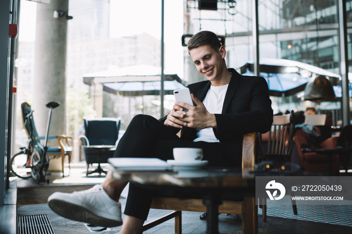 Positive male entrepreneur browsing mobile phone in cafe