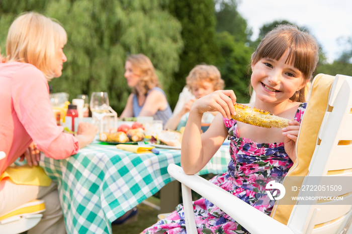 与家人在露台午餐时享用玉米棒的快乐女孩肖像