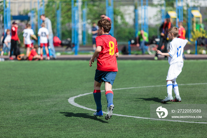 穿着红色运动服的青少年在球场上踢足球，运球。年轻的足球运动员带球