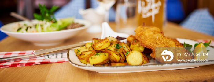 Saftiger Wiener Schnitzel vom Kalb mit wellen Panade und Bratkartoffeln auf schönem Teller