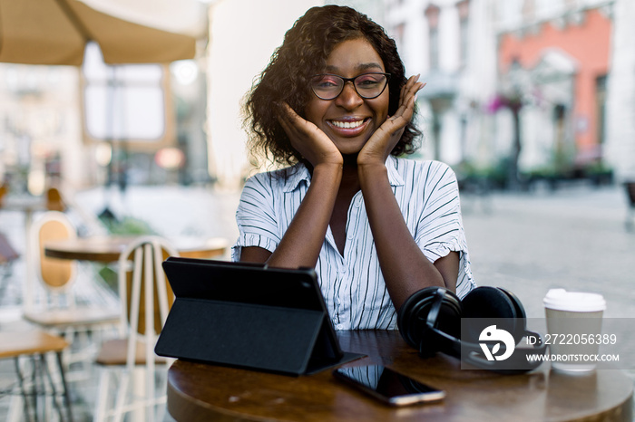 Pretty black business lady , sitting at the table in outdoor city coffee shop, with headphones, smar