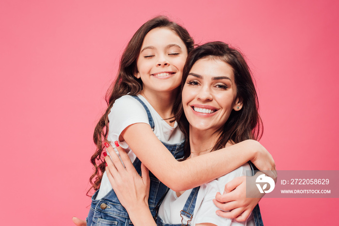 daughter hugging happy mother isolated on pink