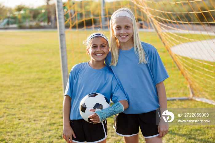 Portrait of smiling girls with ball standing on soccer field