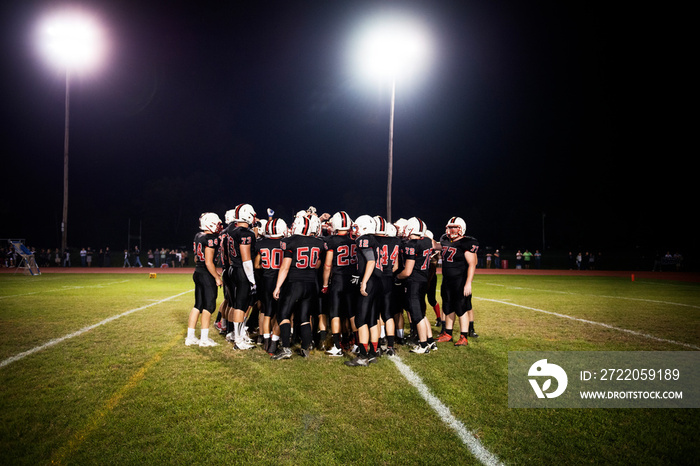 Football players (14-15, 16-17) on playing field ay night