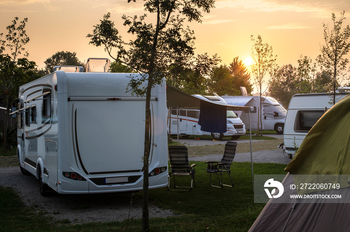 露营地绿色草地上的大篷车和露营者。日出，清晨阳光照在露营者身上。