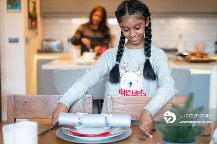 Smiling girl arranging Christmas table setting, mother in background