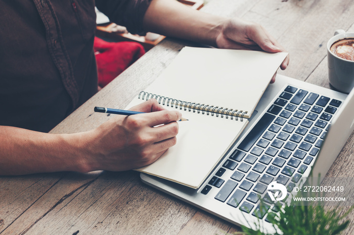 Young business man hand writing notebook and using laptop on wood table.