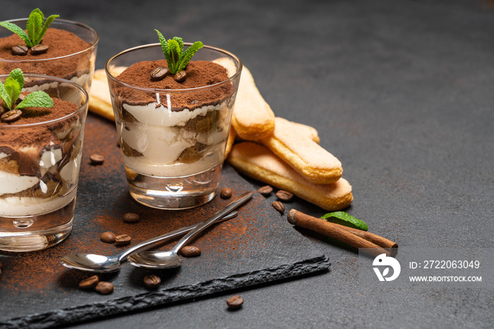 Classic tiramisu dessert in a glass and savoiardi cookies on stone serving board on dark concrete ba