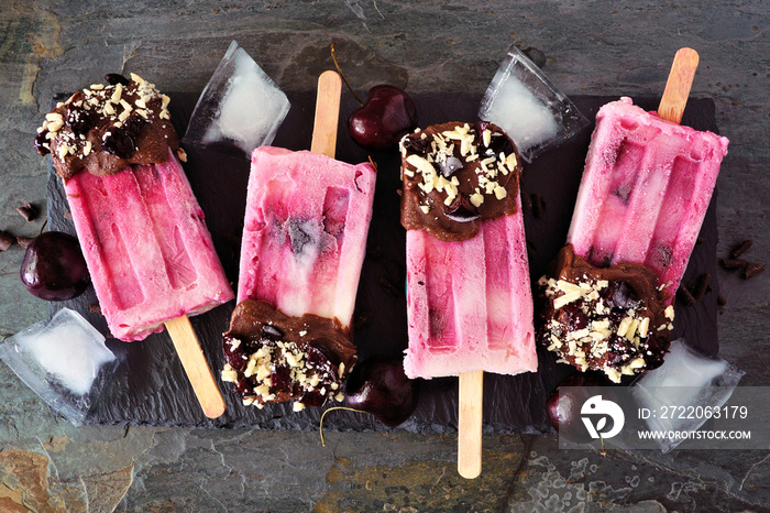 Summer chocolate and nut dipped cherry popsicles. Top view in a row over a dark slate background.