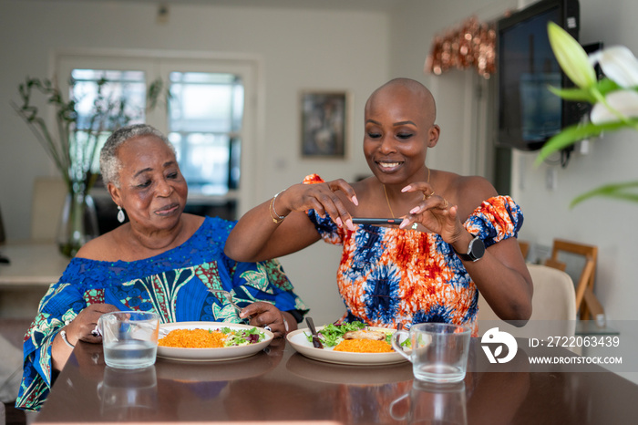 微笑的老年妇女带着成年女儿在餐桌上拍摄食物