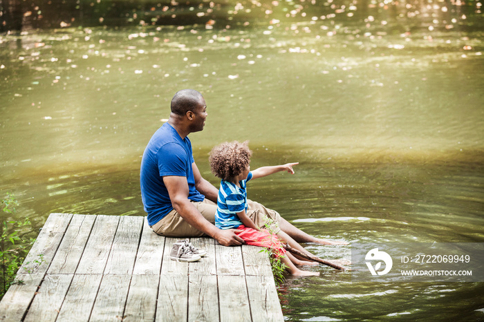 Father and daughter (2-3) dipping feet in river