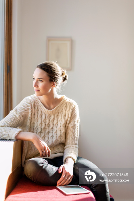 Young woman looking through window while sitting on bench