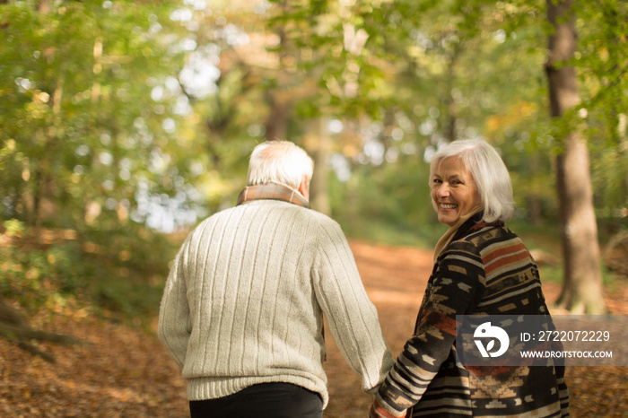 Portrait smiling senior couple holding hands and walking in autumn park