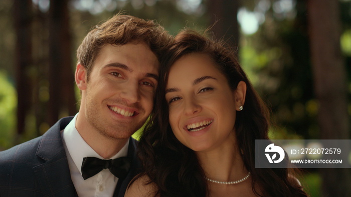 Joyful bride and groom looking at camera in garden. Couple standing in park