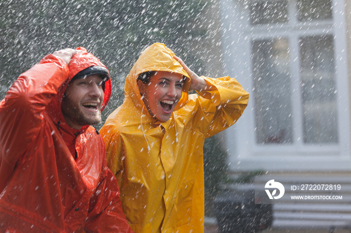 Happy couple in raincoats walking in rain