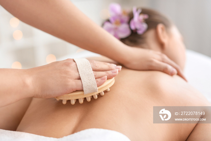 Beautiful young woman receiving massage with brush in spa salon