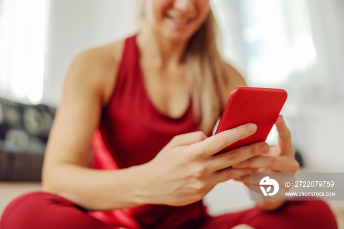 Close up of sportswoman sitting on the floor and using smart phone.