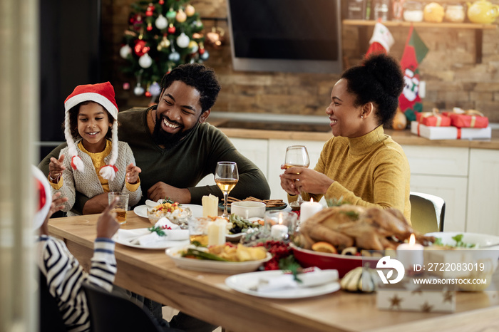 Happy African American family talking during Christmas lunch at dining table.