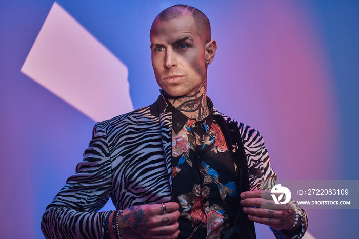 Succesful, daring, tattooed, bald male model posing in a studio for the photoshoot wearing fashionab