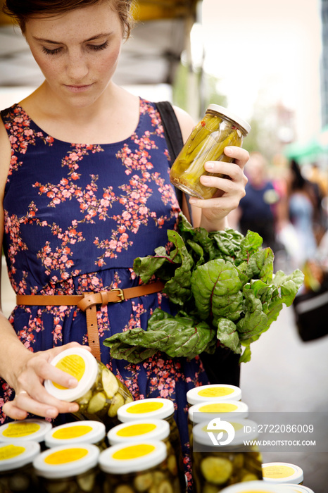 一名妇女在市场上拿着甜菜检查腌黄瓜罐