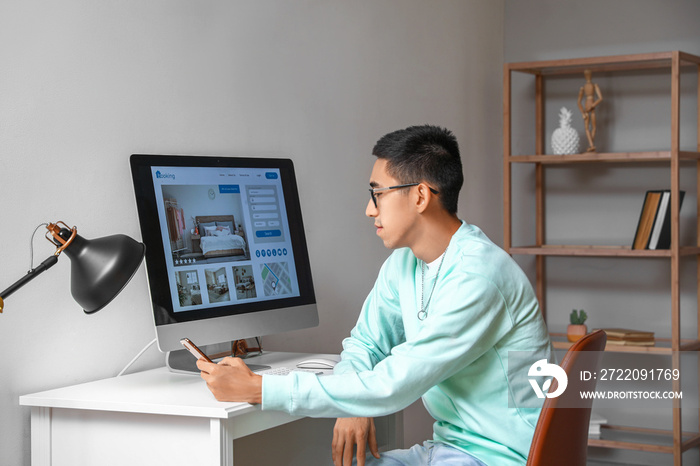 Young man with mobile phone booking hotel room at home