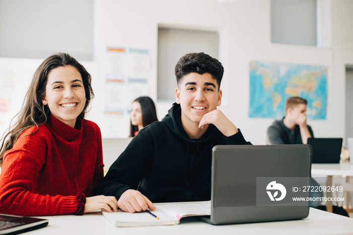 Portrait of smiling teenage friends studying together in classroom at university