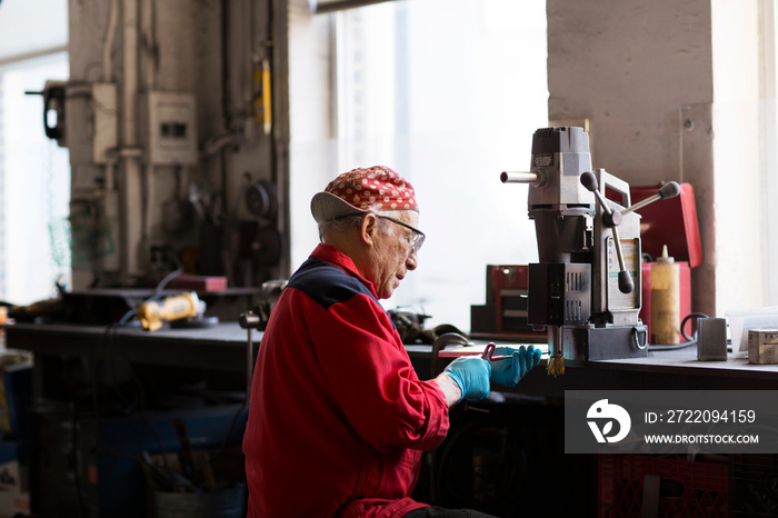 Side view of senior man working on machinery in workshop