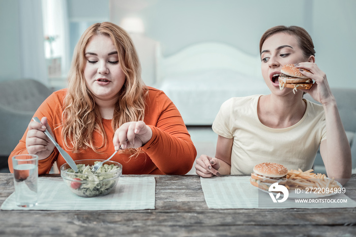 Attentive slim girl looking at plate of her friend