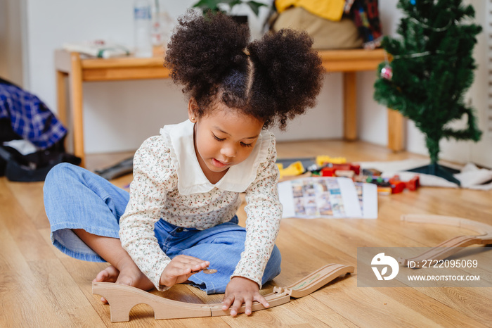 Little girl playing with wooden train tracks at home