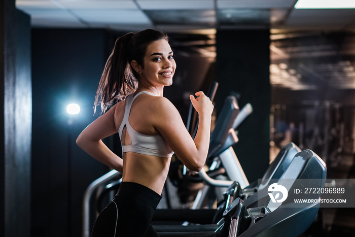 Portrait of a smiling girl in sportswear runing on treadmill in the gym.