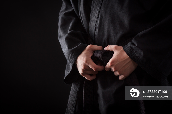 Closeup of male karate fighter hands on the knot of black belt