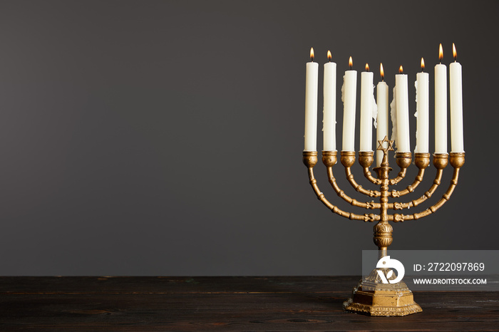 burning candles in menorah on wooden table isolated on grey