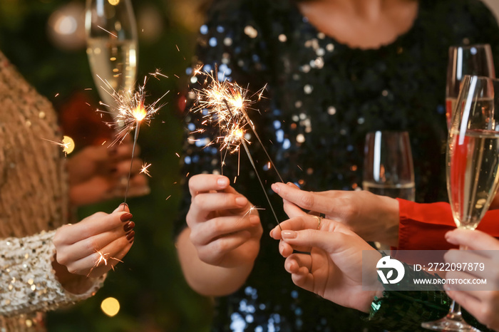 Beautiful young women with sparklers and glasses of champagne celebrating Christmas