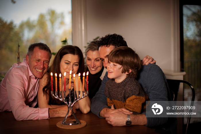 Cheerful multigenerational family looking at lit candles on menorah during Hanukkah