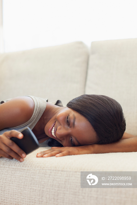 Smiling young woman relaxing on sofa with smart phone