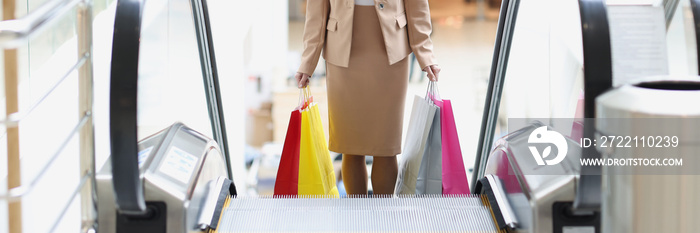 Young stylish woman climbs escalator with shopping bags in shopping center