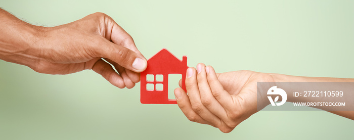 Hands of spouses holding figure of house on green background