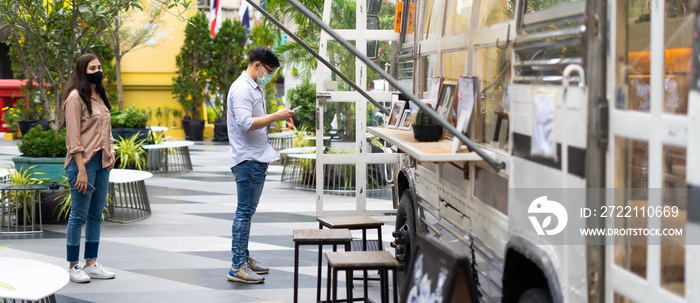 Asian young people wearing face masks stand in line to buy coffee in a multipurpose yard at the city