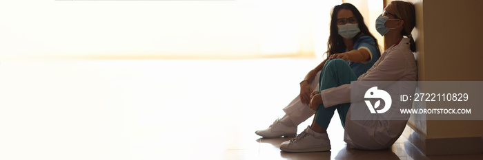 Tired women doctors are sitting in masks in corridor