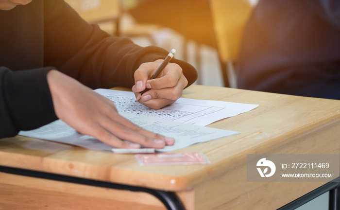 high school or university student hands taking exams, writing examination on paper answer sheet optical form of standardized test on desk doing final exam in classroom. Education  literacy concept.