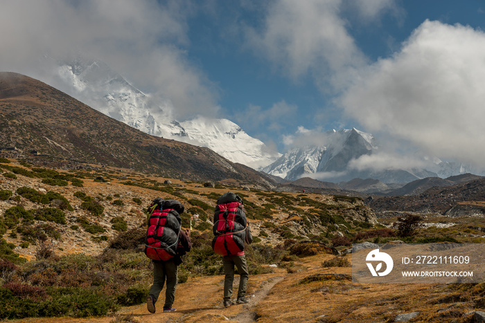 Nepali porters carrying large loads of bags on his back along a track from Dingboche to Everest base camp.