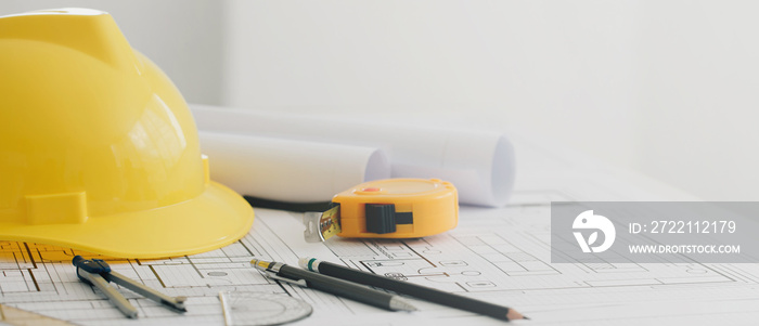 Yellow hard safety helmet hat and the blueprint, pen, ruler, protractor, and tape measure on the table at the construction site.for safety project of workman as engineer or worker.banner copy space.