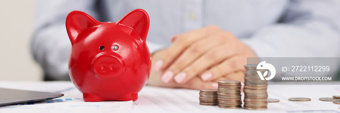 Person accountant on working place, stack of coins, red piggy bank