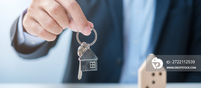 Businessman hand holding key with wooden Home model. Real estate, buy and sale, Property insurance, rental and contract agreement concepts